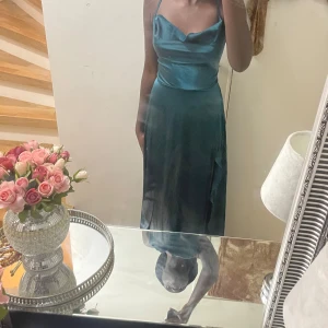 Mörkgrön sidenklänning - Elegant mörkgrön klänning i siden med smala axelband och en vacker snörning i ryggen. Perfekt för en speciell kväll med sin långa, flytande design.