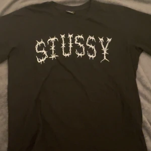 Svart t-shirt från Stussy - Säljer en svart t-shirt från Stussy med ett coolt tryck av taggtråd i vitt på både fram- och baksidan. Gjord av 100% bomull, perfekt för en avslappnad stil. Storlek L. Passar perfekt för streetwear-entusiaster! Passar Baggy för L men bäst för M. Aldrig använd. 