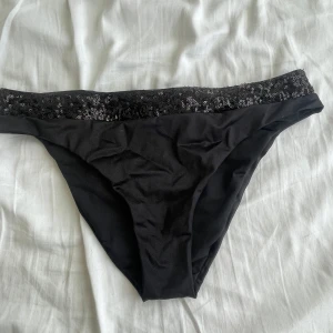 Svarta bikiniunderdelar med paljetter - Svarta bikiniunderdelar från Calzedonia med snygg paljettkant upptill som ger extra glans. Klassisk modell med låg midja och stretchigt material som sitter skönt. Perfekt för strandhäng eller poolparty.