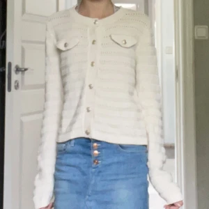 Vit stickad kofta från Vero Moda - Säljer en vit stickad kofta från Vero Moda med snygga guldfärgade knappar och två dekorativa bröstfickor. Koftan har lång ärm, rund halsringning och ett diskret randigt mönster i stickningen. Perfekt att slänga över en topp för en chill look. Pris går att diskuteras 