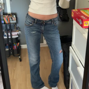 Blå bootcut jeans med broderade fickor - Säljer ett par blå bootcut jeans med låg midja och slitningar på låret och knät. Snygga broderade detaljer på bakfickorna och lite extra detaljer. Skriv privat för mer bilder & frågor 💗