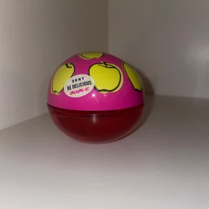 DKNY Be Delicious Orchard St parfym - Säljer en cool parfym från DKNY, Be Delicious Orchard St. Flaskan är rund med rosa och röd färg, dekorerad med gula äpplen på locket. Perfekt för dig som gillar fruktiga och lekfulla dofter. Flaskan är i plast och sticker verkligen ut i badrumshyllan.