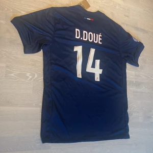PSG 24/25 T-shirt  - •Hej! Säljer en jätte snygg PSG fotbolls T-shirt med Doué på ryggen ⚽️👕 •Den är inte använd bara testad.  •Passar perfekt nu på sommaren ☀️.  •Det är storlek 2xl men tror den passar XL också . •Måtten är på dem sista bilderna 📐.  •Priset kan diskuteras och skickar inom 24 Tim😊