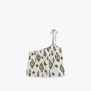 Mönstrad oneshoulder topp med knyt - Supersnygg oneshoulder topp i vitt med svart mönster och en flätad axelrem som knyts. Luftig och lätt i materialet, perfekt för varma dagar. Den har en lös passform och coolt grafiskt mönster som sticker ut.