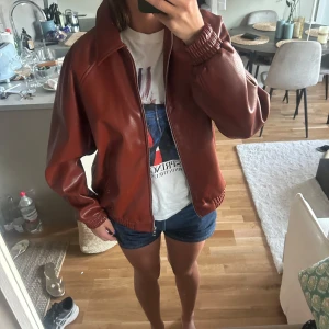 Skinnjacka med dragkedja - Säljer en skinnjacka i klassisk bombermodell med dragkedja framtill och elastiska muddar vid ärmslut och midja. Jackan har en loose passform och är perfekt för dig som gillar en chill och stilren look. Passar till både jeans och shorts. Aldrig använd men lappen är inte kvar, nypris 600kr 