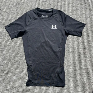Svart kompressionst-shirt Under Armour - Helt ny och aldrig använd svart kompressionst-shirt från Under Armour med korta ärmar och diskret logga på bröstet. Tillverkad i stretchigt syntetmaterial som andas, perfekt för träning. Sitter tight mot kroppen och har sportig look med markerade sömmar. Nypris: 500kr på sportshoppen. Mitt Pris 200kr. 