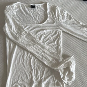 Vit långärmad topp från Gina Tricot - En basic vit långärmad topp från Gina Tricot med rund, djup ringning. Tillverkad i mjuk bomull som känns skön mot huden. 