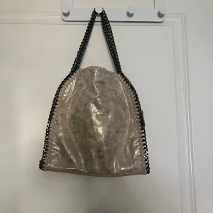 Beige axelväska med kedjedetaljer - Snygg beige/guldig axelväska med glansig yta och kedjehandtag ❤️‍🔥finns även en längre kedja till 🙌