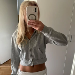 Grå croppad ziphoodie från Brandy Melville - Säljer en ljusgrå croppad ziphoodie från Brandy Melville. Tröjan har dragkedja, snörning och två fickor framtill. Mjuk bomullskänsla och långärmad modell. Nypris 399