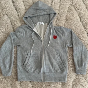 Grå hoodie från Comme des Garçons Play - Grå hoodie med dragkedja från Comme des Garçons Play. Köpt på NK