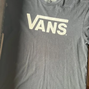 Svart Vans t-shirt med logga - Svart t-shirt från Vans i storlek Large med stor vit Vans-logga på bröstet. Klassisk rund halsringning och korta ärmar. Tillverkad i mjuk 100% bomull som är skön att ha på sig hela dagen. 