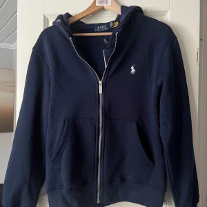 Marinblå hoodie från Polo Ralph Lauren - Säljer helt ny Polo Ralph lauren hoddie. Storlek S säljer pga fick i present och han inte skicka tillbaka. Prislapp och finns kvar. Hör av er vid frågor och funderingar.
