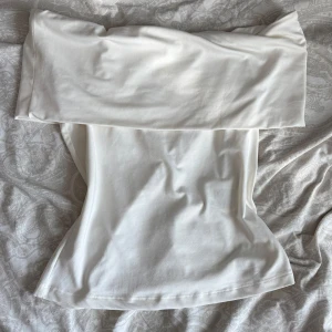 Vit off shoulder top H&M  - Snygg vit axelbandslös tubtopp från H&M i storlek S. Toppen har en bred överdel som ger en cool bandeau-look och är tillverkad i mjukt, stretchigt material. Perfekt att styla med jeans eller kjol för en clean och fräsch vibe. Använd endast en gång. 