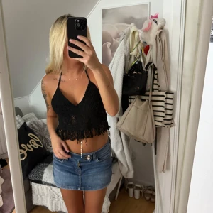 Svart virkad croppad linnetopp - Säljer en svart virkad croppad linnetopp med smala axelband och snygg knytning i ryggen. Toppen har v-ringning och fransdetaljer längst ner för en boho-vibe. Perfekt för varma dagar och festivaler!