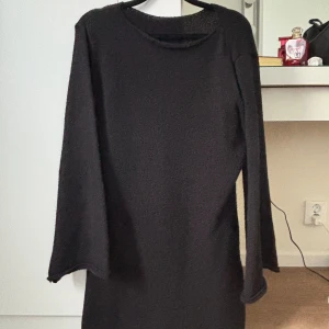 Svart stickad långärmad klänning - En svart stickad klänning med lång ärm och rak passform. Klänningen har en enkel, rund halsringning och är tillverkad i ett mjukt, grovstickat material. Perfekt för dig som gillar minimalistisk och stilren look.