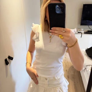 Vit topp med volangdetaljer - Supersöt vit topp med volangdetaljer på armarna! Är sparsamt använd och därför i väldigt bra skick, inga defekter! Säljer pågrund av att den inte används💗
