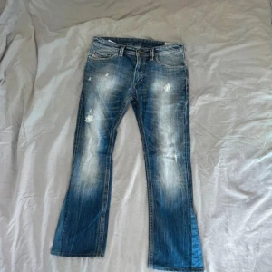 Diesel jeans blå  - Snygga blå bootcut jeans från Diesel med slitningar och ljusa partier framtill. Klassisk femficksmodell med låg midja och tydlig tvättad look. Perfekta för dig som gillar en avslappnad och trendig stil.
