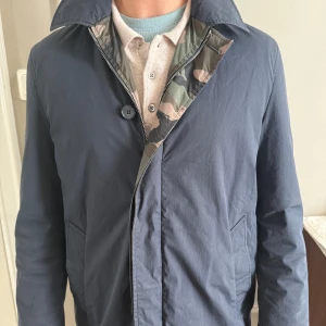 Vändbar  valentino vindjacka med camomönster - Säljer en vändbar Valentino vindjacka med ena sidan i mörkblått och andra sidan i klassiskt camouflage. Jackan har dragkedja, hög krage och sidfickor. Perfekt för dig som vill kunna variera din stil snabbt. Materialet är  lätt och smidigt.