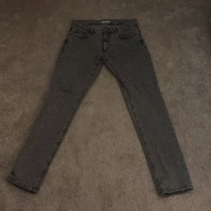 Grå jeans från Woodbird, storlek 30/34 - Säljer ett par grå jeans från Woodbird i storlek 30/34. Jeansen har en klassisk femficksdesign, raka ben och normal passform. Materialet är bomull och färgen är tvättad grå. Litet slitage längst ner då de är lite slitna där.