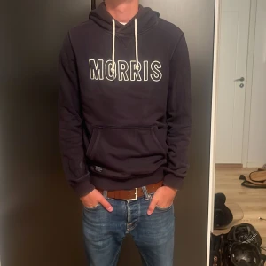  Morris hoodie - Svart hoodie från Morris med vit broderad logga på bröstet och vita snören i huvan. Klassisk känguruficka framtill och mjukt material som känns skönt mot huden. Perfekt för en chill och avslappnad stil. Priset är inte hugget i sten så hör gärna av er vid intresse 