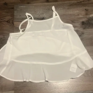 Vit linnetopp från NA-KD - Säljer en vit, luftig linnetopp från NA-KD i storlek 32. Toppen har tunna axelband och volangkant nertill, vilket ger en söt och flowy look. Perfekt för varma dagar och enkel att styla med jeans eller kjol.