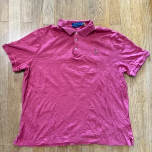 Rosa pikétröja Polo Ralph Lauren XL - Klassisk rosa pikétröja från Polo Ralph Lauren i bomull. Tröjan har krage, tre knappar och den ikoniska broderade loggan på bröstet. Classic fit-modell med korta ärmar, perfekt för en chill och stilren look.