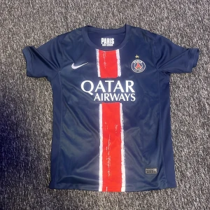 PSG matchtröja D. Doué #14 Nike - Paris Saint-Germain fotbollströja med D. Doué och nummer 14 på ryggen. Mörkblå med röd och vit rand på framsidan, PSG-emblem och Nike-logga. Tillverkad i Dri-FIT-material som andas. Snygg och sportig design för dig som älskar fotboll.