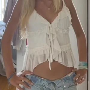 Vit volangig blus med knyt - Supersöt vit blus med volanger och knyt framtill. Luftigt, transparent tyg med romantiska detaljer och v-ringning. Perfekt för en somrig look och passar till både jeans och kjol. Axelbandsmodell och flowig passform. Storlek M men passar mig som har Xs och S❤️