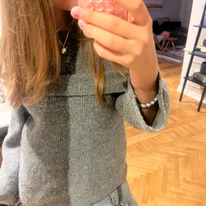 Grå stickad tröja med vida ärmar - Mysig grå stickad tröja med bred krage och vida, långa ärmar. Tröjan har en avslappnad passform och är perfekt att styla med jeans eller kjol. Enkel men ändå trendig look för höst och vinter.