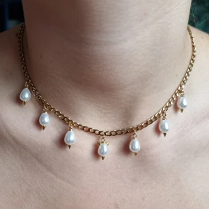Guldfärgat halsband med pärldroppar - Stilrent halsband med chunky guldfärgad kedja och sju droppformade vita pärlor som hänger längs kedjan. Rostfrit stål, glaspärlor. Längd-40cm,kedjetjocklek-4cm 