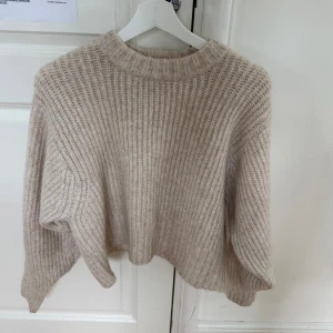 Beige stickad tröja från Monki - Supermysig beige stickad tröja från Monki med grov ribbstickning och rund hals. Tröjan har en relaxed passform och långa ärmar. Enkel att matcha med både jeans och kjol.