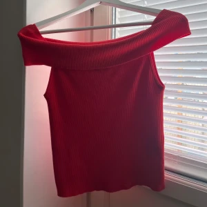 Röd ribbad offshoulder topp Vero Moda - Säljer en snygg röd ribbad topp från Vero Moda med bred offshoulder-krage. Toppen är ärmlös och har en tight passform som framhäver axlarna. 