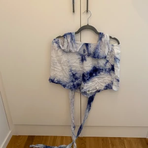 Blåvita tie-dye shorts med knytning så att det blir en playsuit - Unika blåvita shorts med tie-dye mönster och långa knytband i midjan som man knyter upp så att det blir en body. Man kan knyta på många olika sätt och kan på de viset få flera plagg i ett Lätta och luftiga, perfekta för varma dagar. De har en loose passform.
