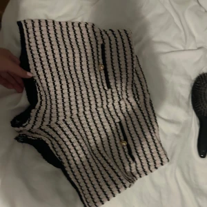 Randiga beige och svarta shorts - Snygga shorts i beige och svart med randigt mönster och dekorativa guldknappar på fickorna. De har en lite tjockare, stickad känsla och är perfekta för dig som vill sticka ut med en trendig look. Skriv om ni vill va fler bilder