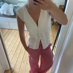 Vit blus med v-ringning och knappar - Säljer en vit blus med djup v-ringning och knäppning framtill. Blusen är ärmlös och har fina sömdetaljer längs midjan som ger en snygg siluett. Perfekt till jeans eller kjol för en fräsch look. Materialet känns lätt och luftigt. Hemsydd xs eller s skulle ja söga