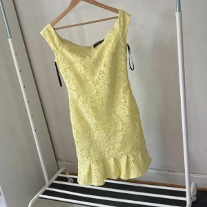 Gul spetsklänning från Paper Dolls - Superfin gul kortklänning från Paper Dolls med spetsdetaljer och volang nertill. Klänningen har en figurnära passform, är ärmlös och stängs med dragkedja bak. Perfekt för dig som vill sticka ut med en ljus och somrig look!