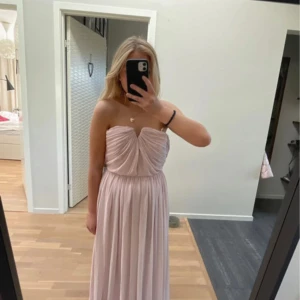 Ljusrosa axelbandslös långklänning - Säljer en romantisk ljusrosa balklänning med axelbandslös design och draperad överdel. Klänningen har en mjukt fallande kjol och markerad midja, perfekt för speciella tillfällen.