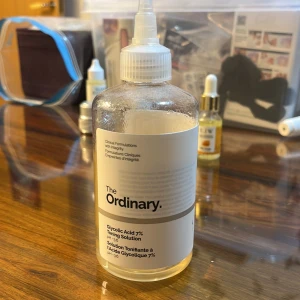 The Ordinary Glycolic Acid 7% Toning Solution - En stor flaska ansiktsvatten från The Ordinary med 7% glykolsyra. Produkten är genomskinlig med vit etikett och svart text. Perfekt för exfoliering och att fräscha upp huden. Kommer i plastflaska med skruvkork och pipett.