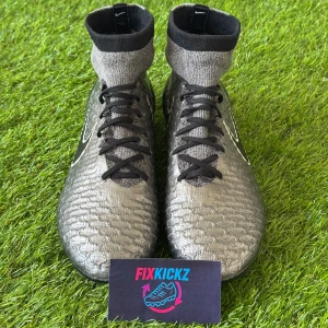 Nike Magista Obra Silver - Säljer ett par Nike fotbollsskor med högt skaft i silver och svart. Skorna har svart snörning, stickad strumpa runt ankeln och gula dobbar undertill. Perfekta för dig som vill ha bra grepp på planen och snygg design.