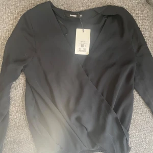 Svart omlottblus från Bik Bok - Säljer en svart omlottblus från Bik Bok i lätt och luftig polyester. Blusen har långa ärmar och en snygg v-ringning framtill. Aldrig använd