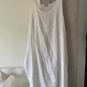 Vit linneklänning - Vit linneklänning i A-formad modell. Ficka på varje sida, men en ficka har hål. Passar fint till stranden.  Köpt i Italien och saknar märke.  Storlek one-size men passar mig som är 36/38 i storlek.