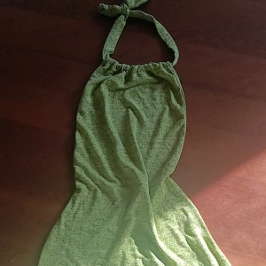 Grön halterneckklänning - Säljer en grön halterneckklänning med knyt i nacken. Klänningen har en mjuk och lätt struktur, perfekt för varma dagar. Enkel och stilren design utan mönster eller extra detaljer. 