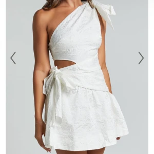 Vit oneshoulder klänning med rosett - Säljer en vit kortklänning med oneshoulder och stor rosett på axeln. Klänningen har en snygg cut-out vid midjan och en extra rosettdetalj på sidan. Perfekt för sommarens alla tillfällen och speciellt studenten! Säljer för att jag valde en annan! 