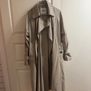 Beige trenchcoat från ZARA - Säljer en klassisk beige trenchcoat från ZARA i storlek XS. Jackan har långa ärmar, knappar framtill, bälte i midjan och detaljer vid ärmsluten. Perfekt för övergångssäsonger och ger en stilren look. Jag har vanligtvis S i jackor och andra överdelar.