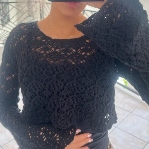 Svart virkad croppad tröja - Säljer en svart virkad croppad tröja med lång ärm och vid passform. Tröjan har ett snyggt spetsliknande mönster och är perfekt att styla över ett linne eller topp. Den går ut vid händerna. Superfin detalj till din outfit! Pris går att diskutera.