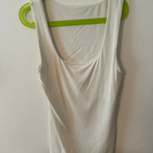 Vit ärmlös linnetopp - Säljer en enkel och stilren vit linnetopp med rundad halsringning. Toppen är ärmlös och har en smickrande passform. Man kan ha den åt vilket håll man vill! Den har ett stretchigt material 