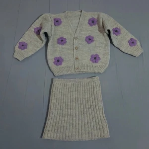 Stickad kjol med lila blommor - Beige stickad kjol med ribbad struktur och dekorativa lila blommor. Kjolen har en rak passform och är perfekt för dig som gillar en mysig och trendig stil.