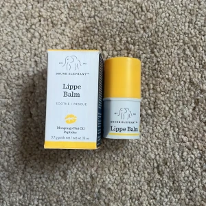 Lippe Balm från Drunk Elephant - Läppbalsam från Drunk Elephant i en söt gul och vit förpackning. Innehåller mongongo-nötolja och peptider för att återfukta och vårda läpparna. Kompakt och smidig att ta med i väskan.