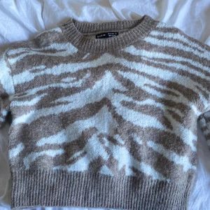 Beige och vit zebramönstrad stickad tröja från SHEIN - Supermjuk stickad tröja från SHEIN i beige och vitt zebramönster. Tröjan har rund halsringning, långa ärmar och bred ribbad mudd vid nederkant och ärmslut. Perfekt för att lyfta din vardagsstil!