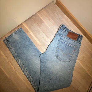 Ljusblå replay  - Klassiska ljusblå replay jeans med raka ben och femficksmodell. Jeansen har en brun läderpatch bak i midjan och är tillverkade i slitstarkt denim. Perfekta för en avslappnad och tidlös stil. Storlek 30/31